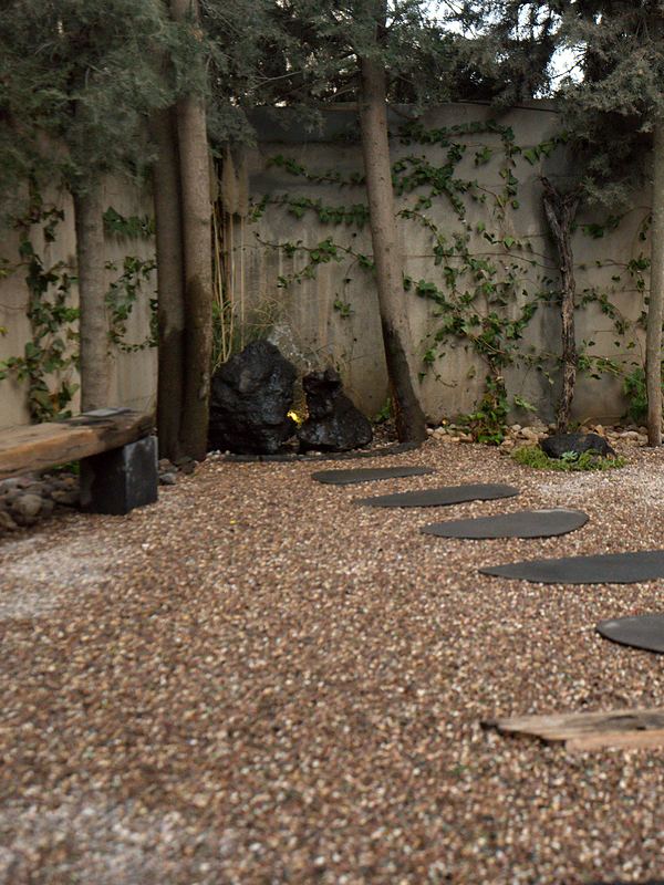 The courtyard at dusk: a garden light glows between black boulders, beside a timber bench and a line of basalt stepping stones.